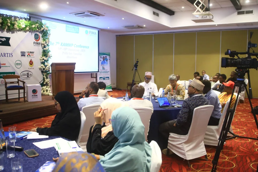 Members working through a session at round tables in the conference hall, sponsor banners and a camera behind them, 2025