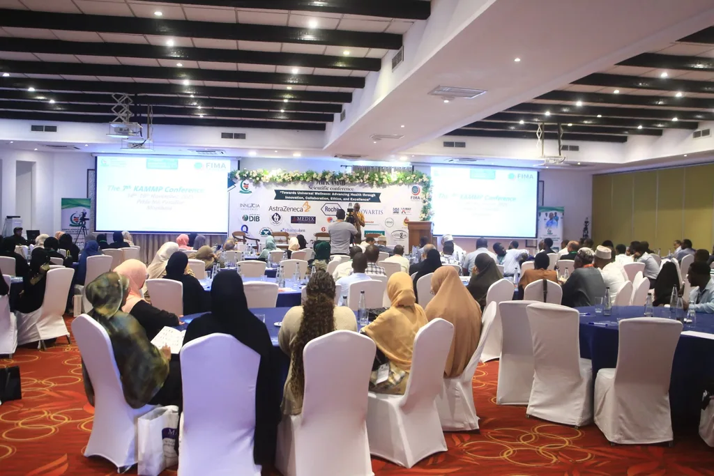 The plenary hall of the 7th KAMMP Scientific Conference, delegates at round tables facing the stage and the conference banner, Mombasa 2025