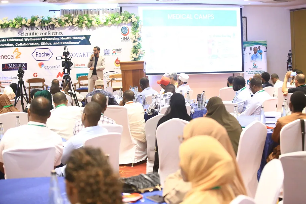 A plenary session at the 7th KAMMP Scientific Conference: delegates follow a presentation on the screens beside the conference banner, 2025