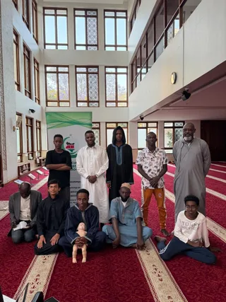 Participants of a KAMMP life-support training gathered in a mosque beside the association banner, a training manikin in front