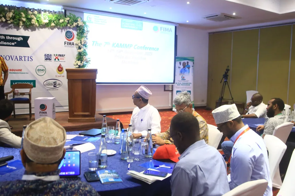 Delegates at the front tables during a talk at the 7th KAMMP Scientific Conference, the lectern and banners behind, 2025