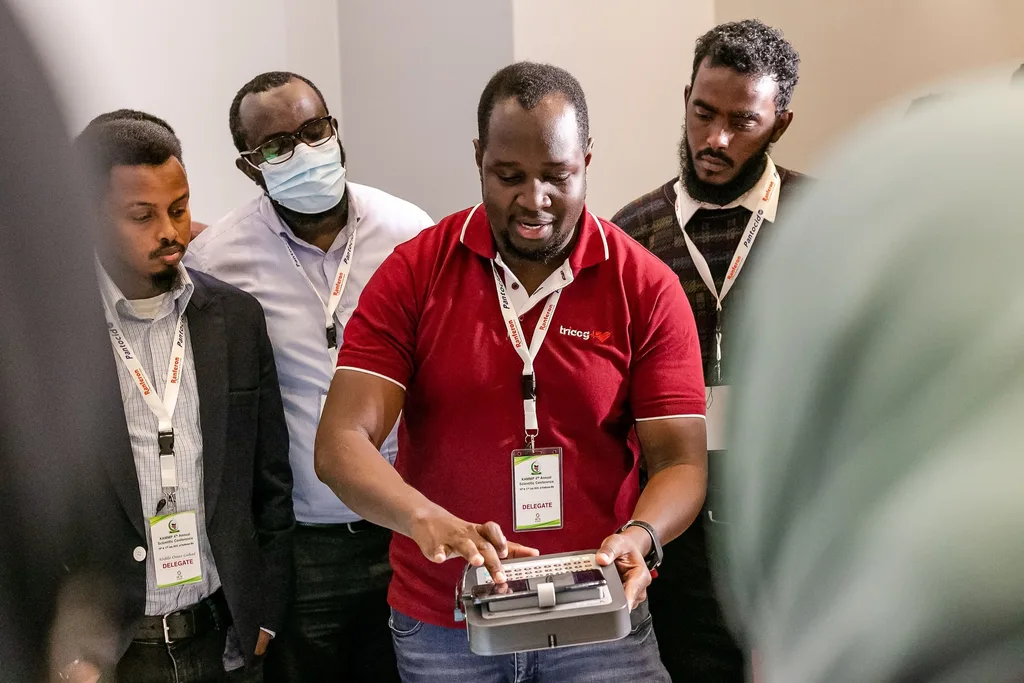 A hands-on skills station at the 4th KAMMP conference: a facilitator demonstrates a device to delegates, Nairobi 2022